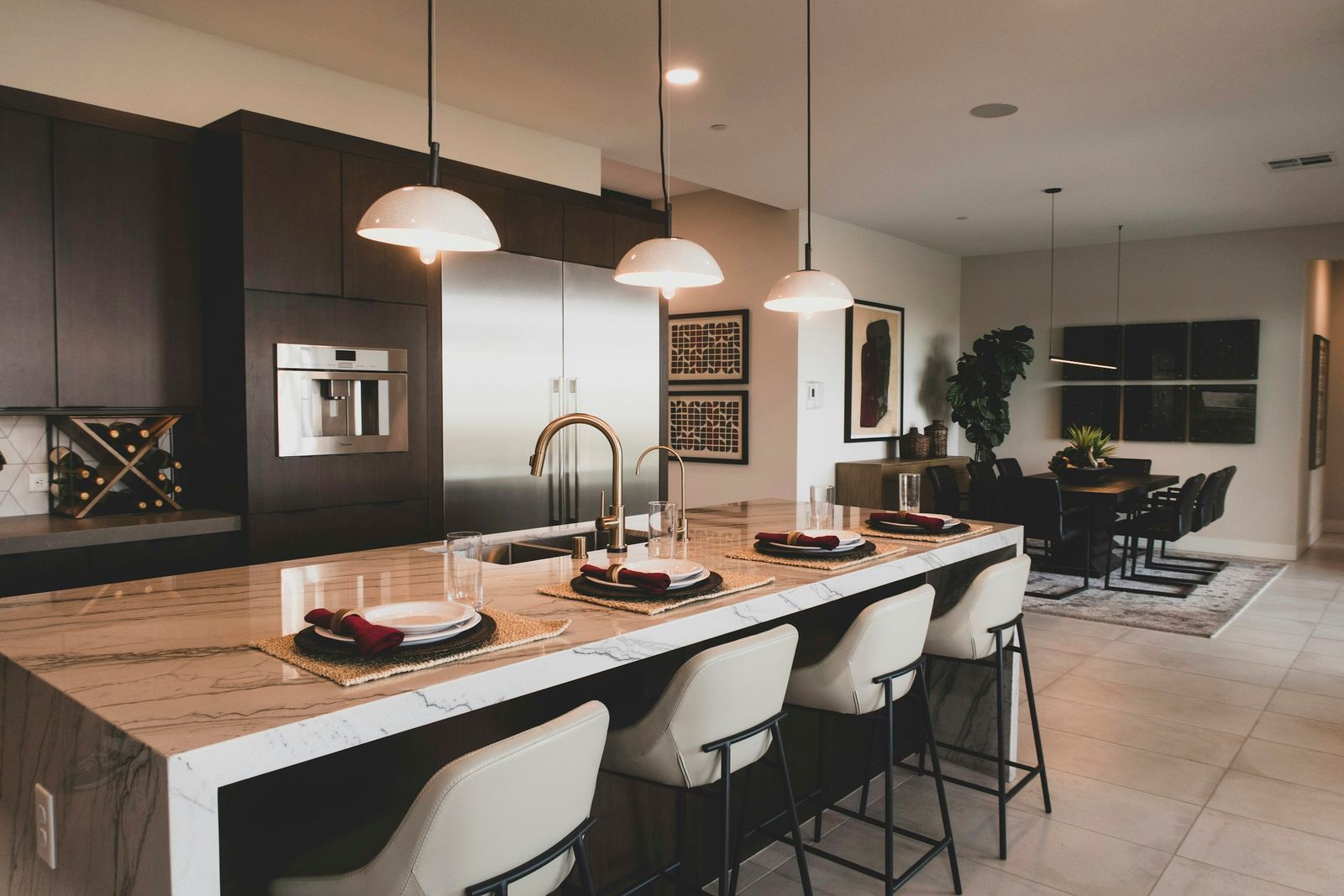 Modern kitchen with a long waterfall-marble island under three white dome pendants and a grid of recessed downlights, dark flat-panel cabinets behind