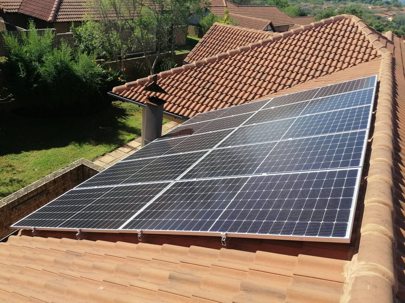 Array of black solar panels mounted on a terracotta barrel-tile roof on a sunny day