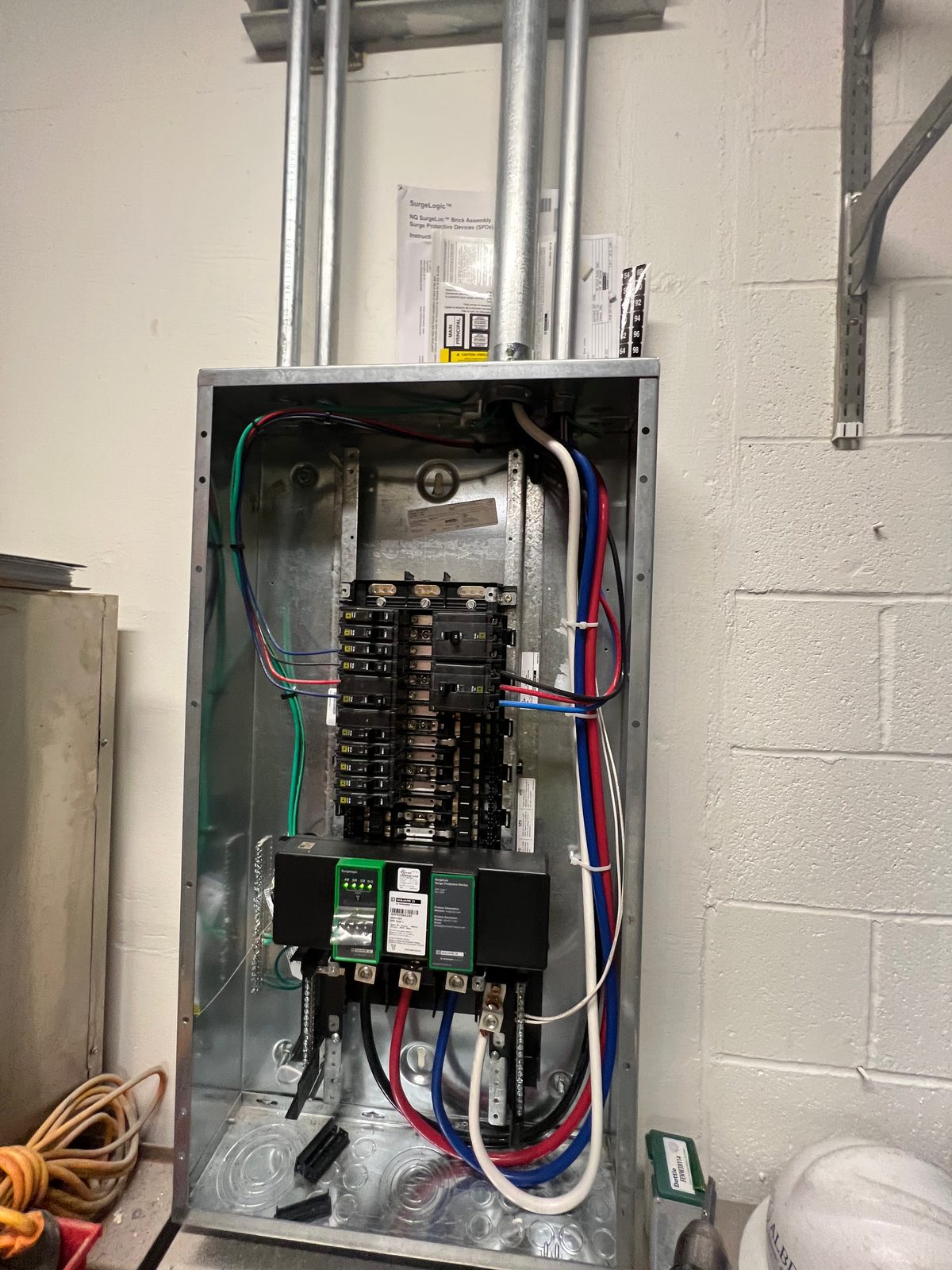 Commercial panel with the dead-front removed showing breakers, color-coded conductors and conduits entering from the top, against a block wall