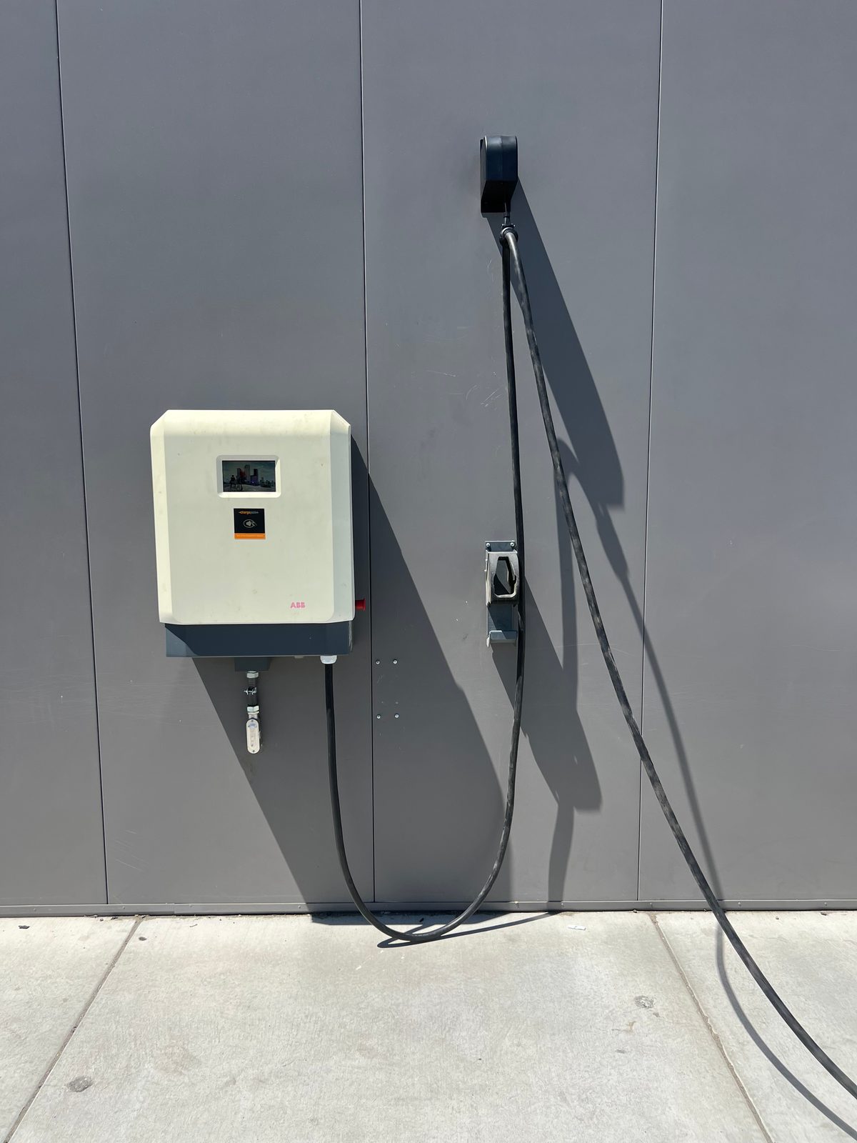 Wall-mounted commercial EV charging unit on a gray panel wall with a connector holster and long charging cable