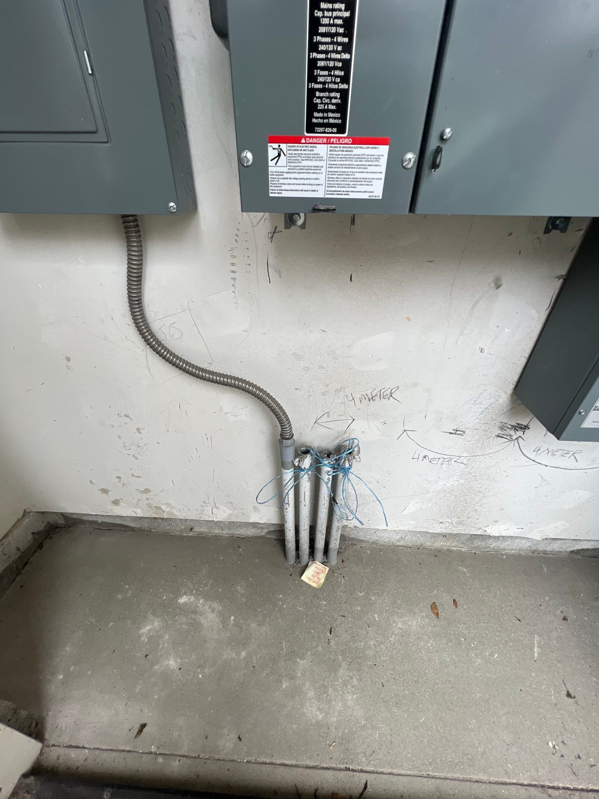 Conduit stub-ups coming out of a concrete floor below a pair of gray panels, with flexible conduit looping down the wall
