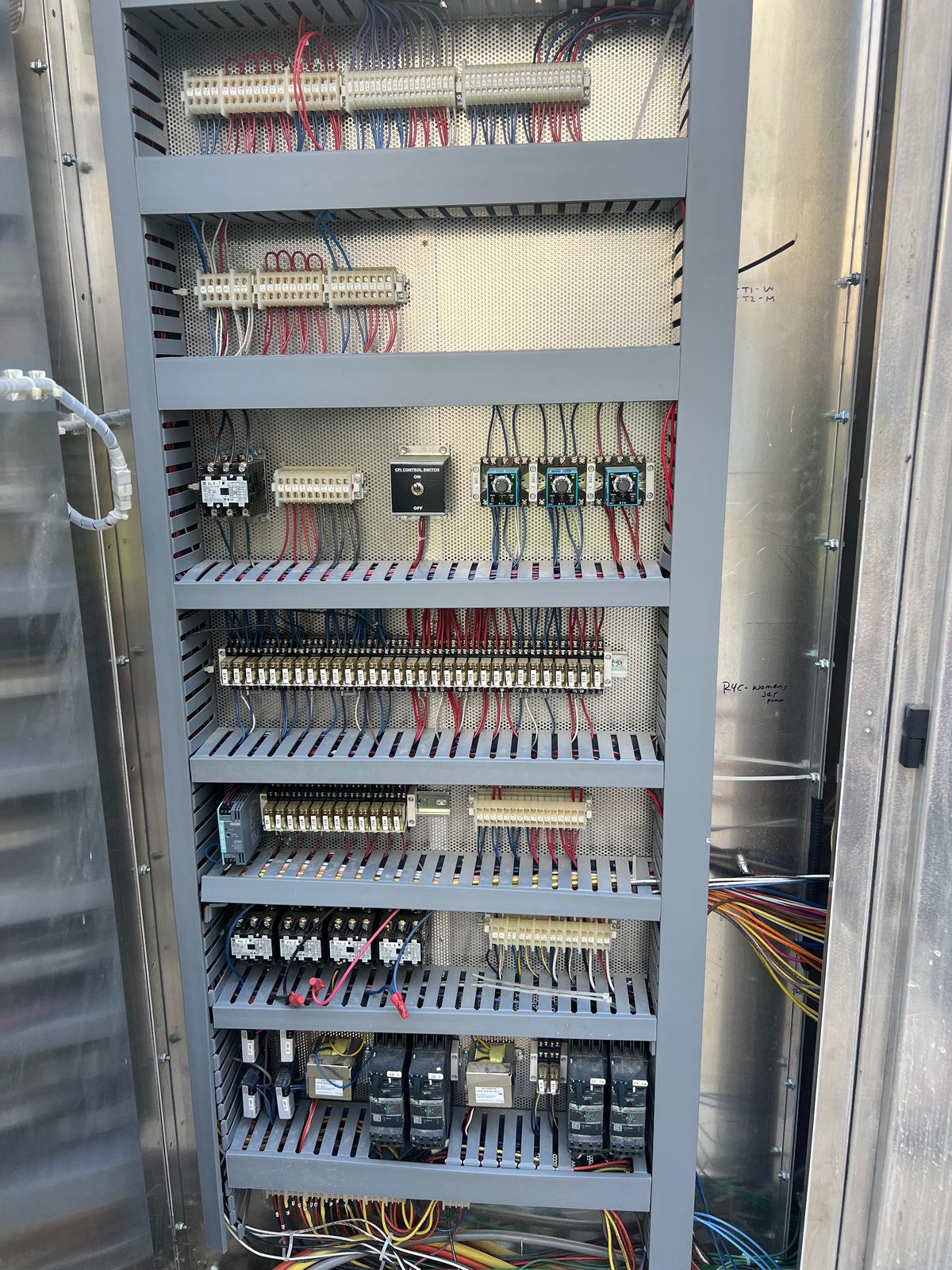 Tall control cabinet with terminal blocks, relays and power supplies mounted on DIN rails and wired through slotted wire ducts