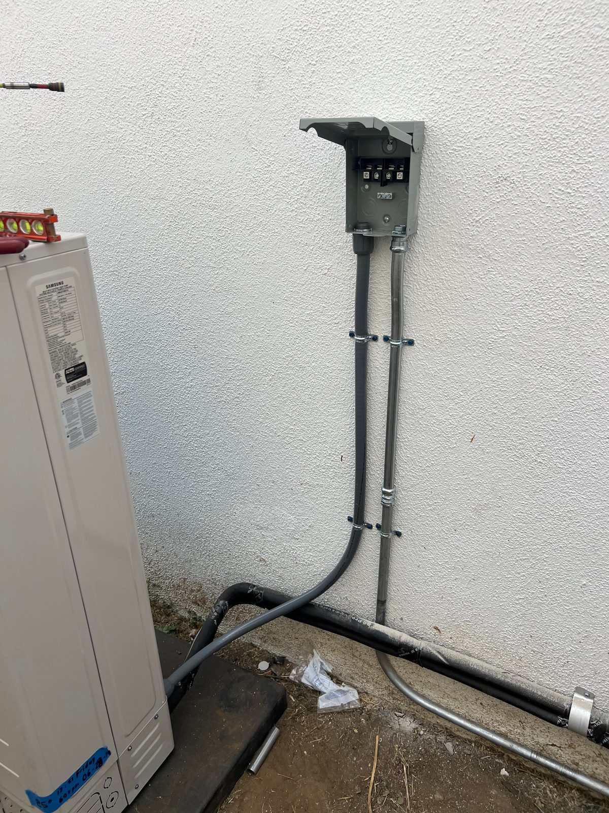 Pull-out disconnect on a white wall with liquidtight flexible conduit running down and across to a tall outdoor equipment cabinet