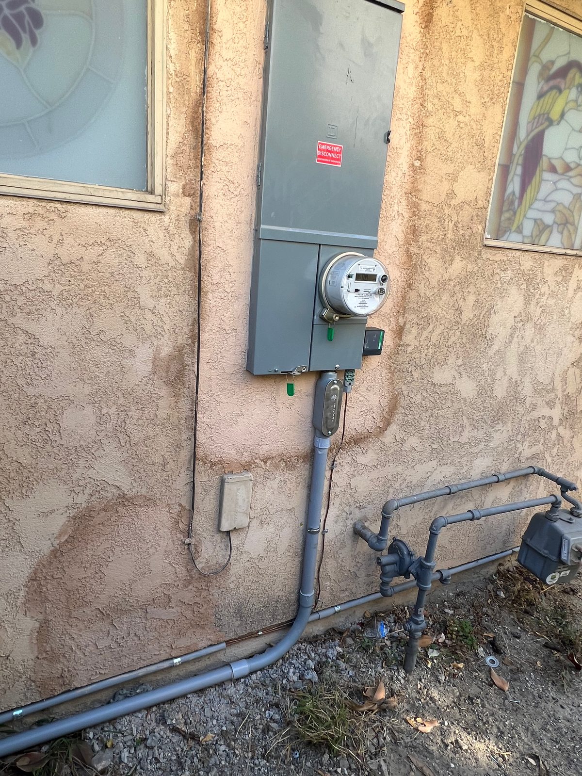 Residential meter panel on a tan stucco wall with gray conduit running down and along the base of the wall