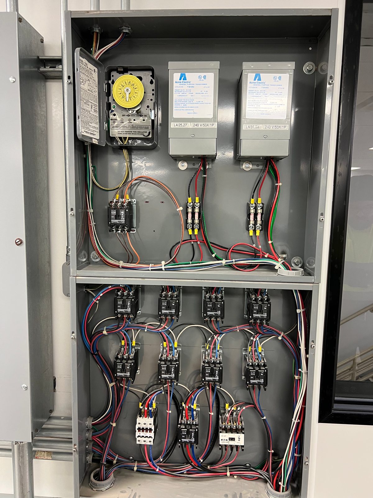 Open control enclosure with a mechanical time clock and transformers on top and eight lighting contactors wired below