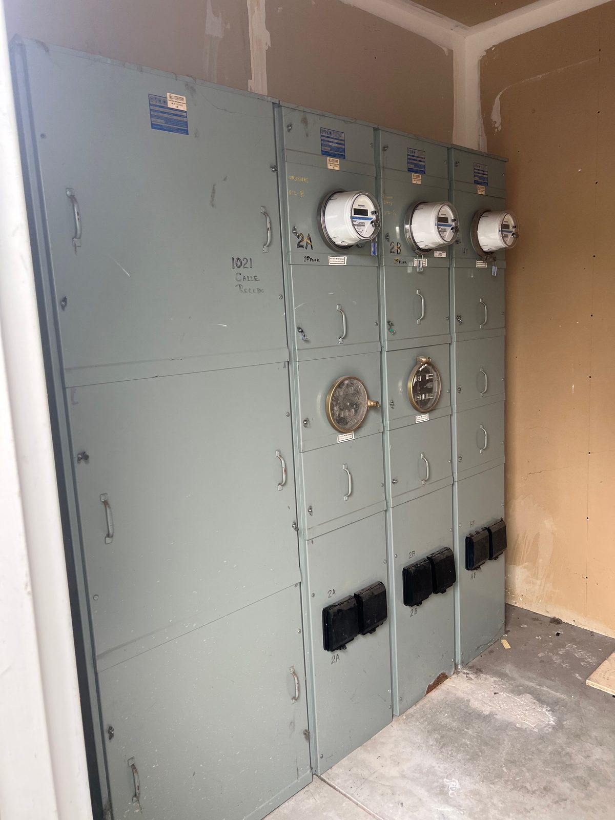 Gray multi-unit meter stack in a utility room with three meters set and unit labels written on the covers