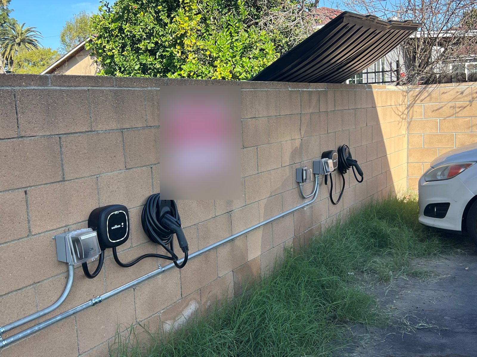 Two wall-mounted EV chargers and their disconnects on a block wall in a parking area, fed by a single EMT conduit run