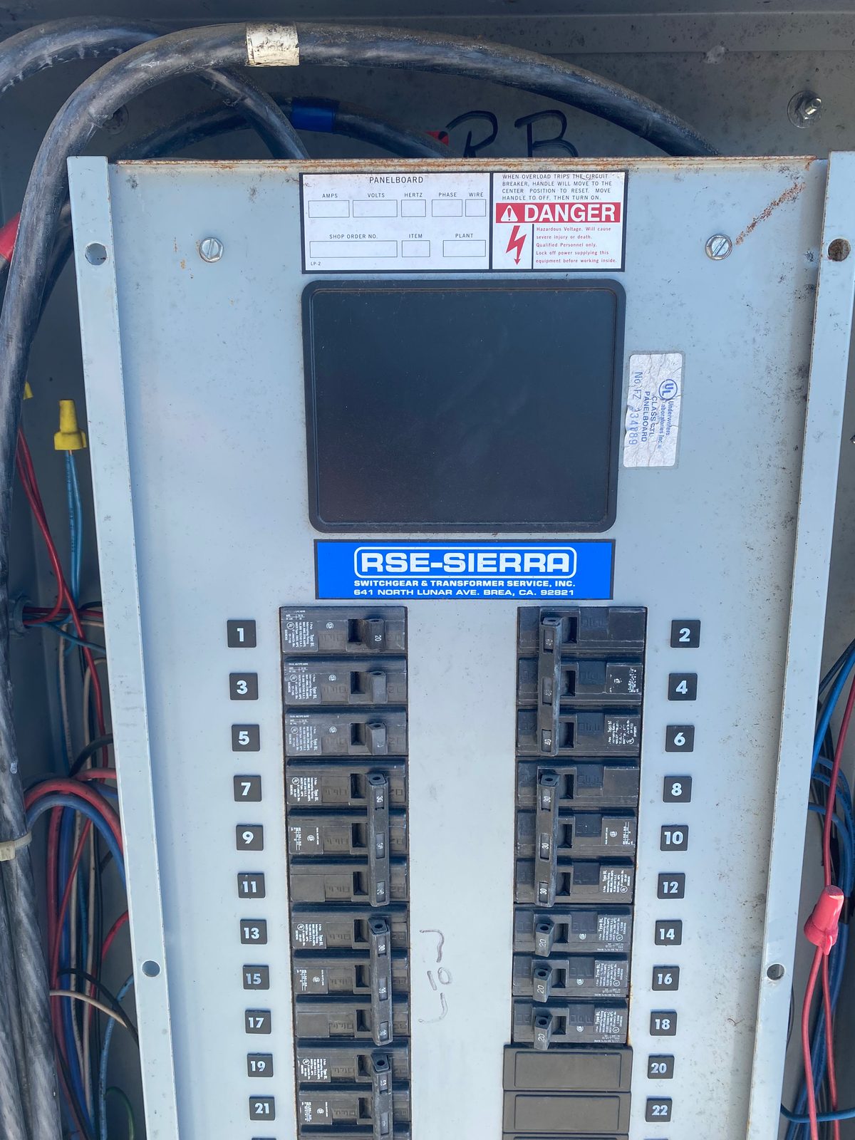 Older gray panelboard with a directory card and two columns of numbered breakers, wires visible around the enclosure