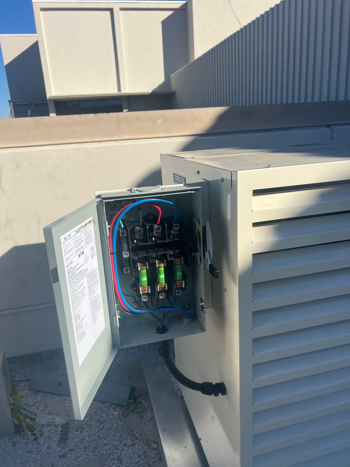 Open fused disconnect switch with three cartridge fuses mounted beside a rooftop HVAC unit