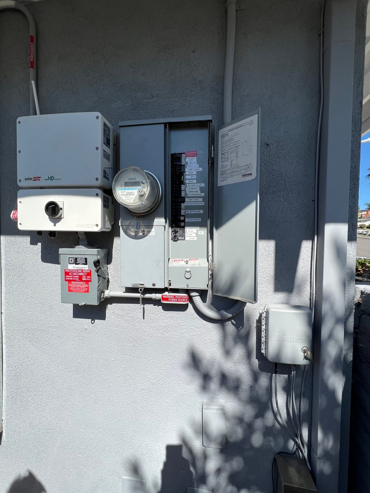 SolarEdge inverter, utility meter, AC disconnect and main panel mounted on a gray stucco wall of a house