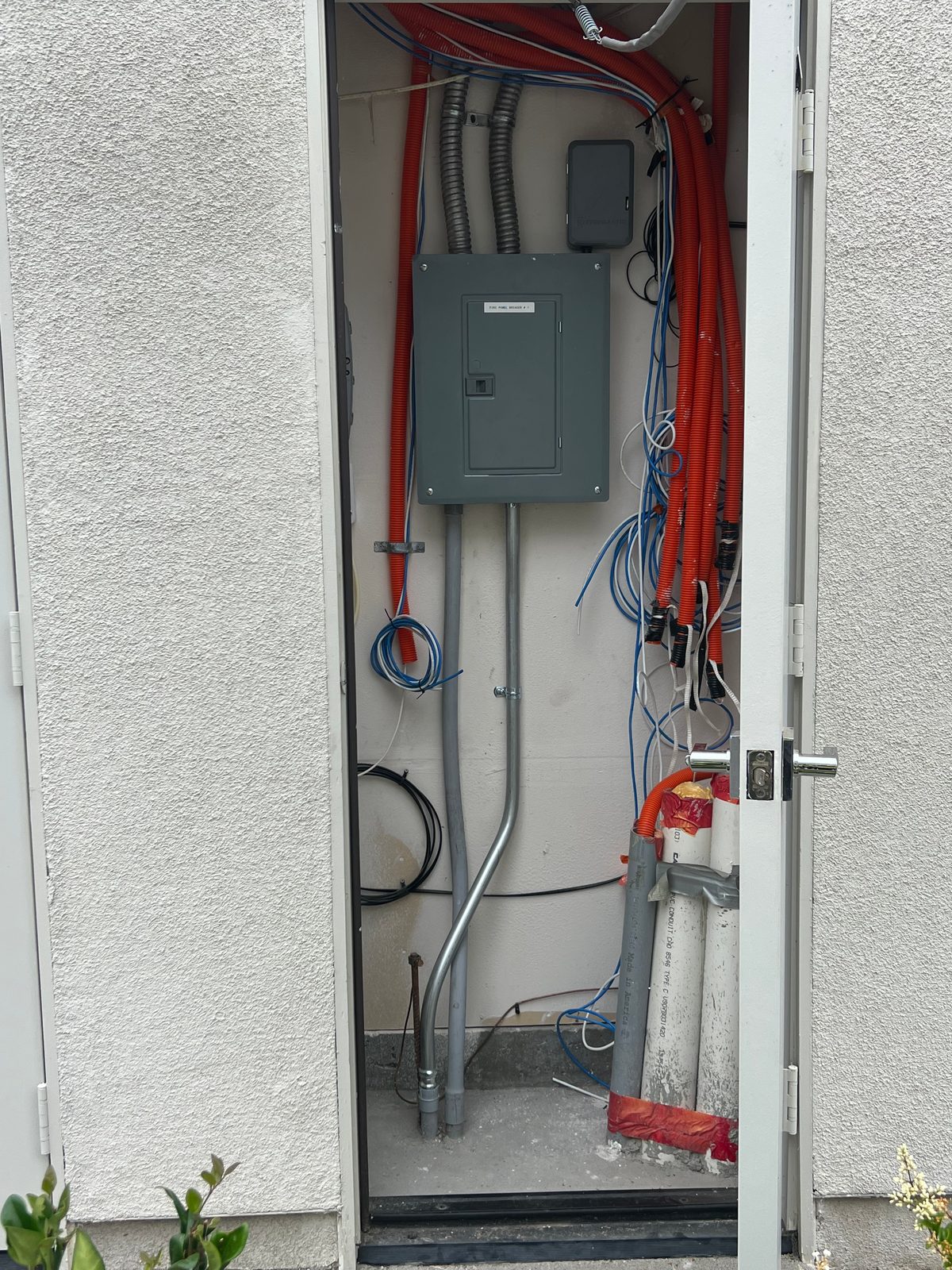 Small panel in an exterior utility closet with orange MC cable and blue low-voltage cable bundled along the side